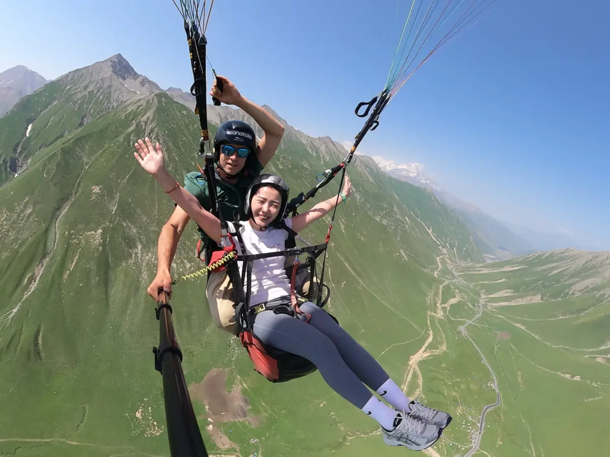 Two paragliders in tandem flight over green mountains near Llogara Pass, Vlora Albania