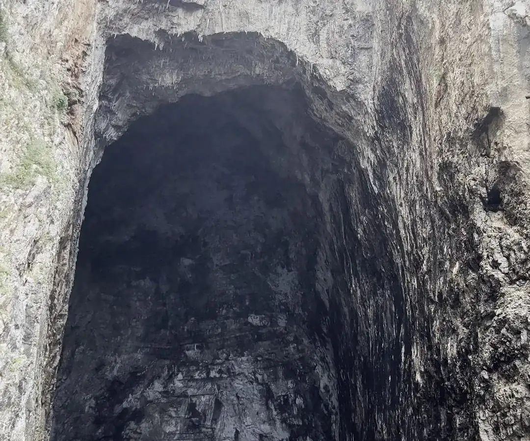 Boat approaching Haxhi Ali Cave entrance through narrow limestone canyon with dark cave opening